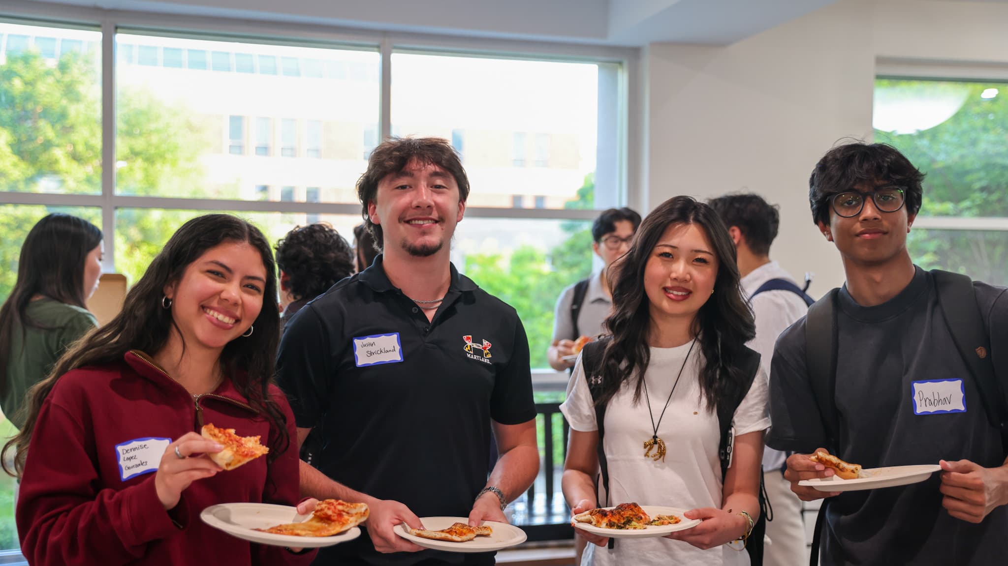 Four students with name tags and plates of food, talking at a DVCG event